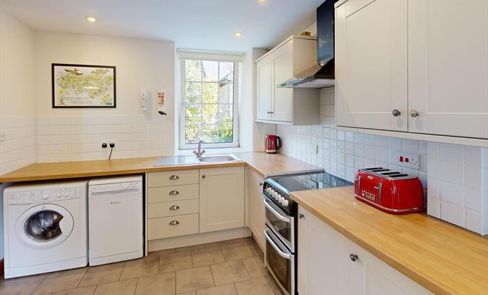 A light-filled kitchen featuring a cooker, wooden worktops, cream shaker cabinets, and essential appliances including washing machine and dishwasher.